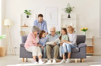 Ein Großvater, der auf dem Sofa sitzt und mit seinen Kindern und Enkelkindern ein Buch anschaut. 